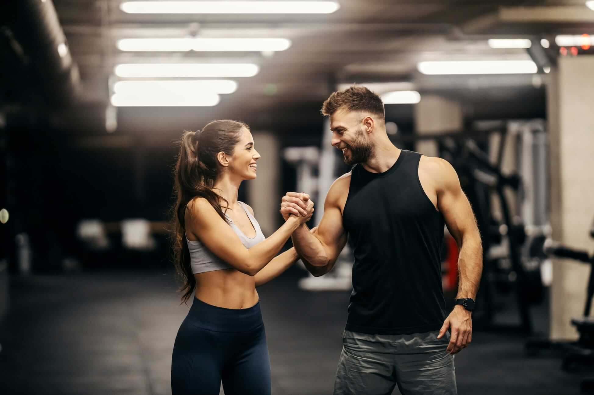 Ein Mann und eine Frau im Fitnessstudio, die sich lachend per Handschlag motivieren, vor einer Kulisse aus Fitnessgeräten. Ein Mann und eine Frau im Fitnessstudio, die sich lachend per Handschlag motivieren, vor einer Kulisse aus Fitnessgeräten.