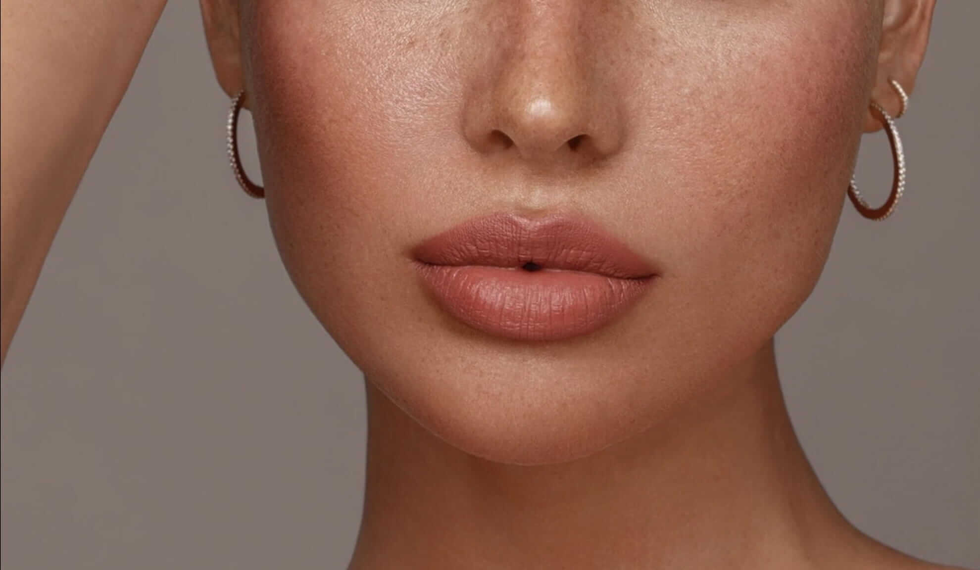 Nahaufnahme von Lippen und Nase einer Frau mit Sommersprossen und dezentem Make-up, ergänzt durch schlichte Ohrringe. Nahaufnahme von Lippen und Nase einer Frau mit Sommersprossen und dezentem Make-up, ergänzt durch schlichte Ohrringe.